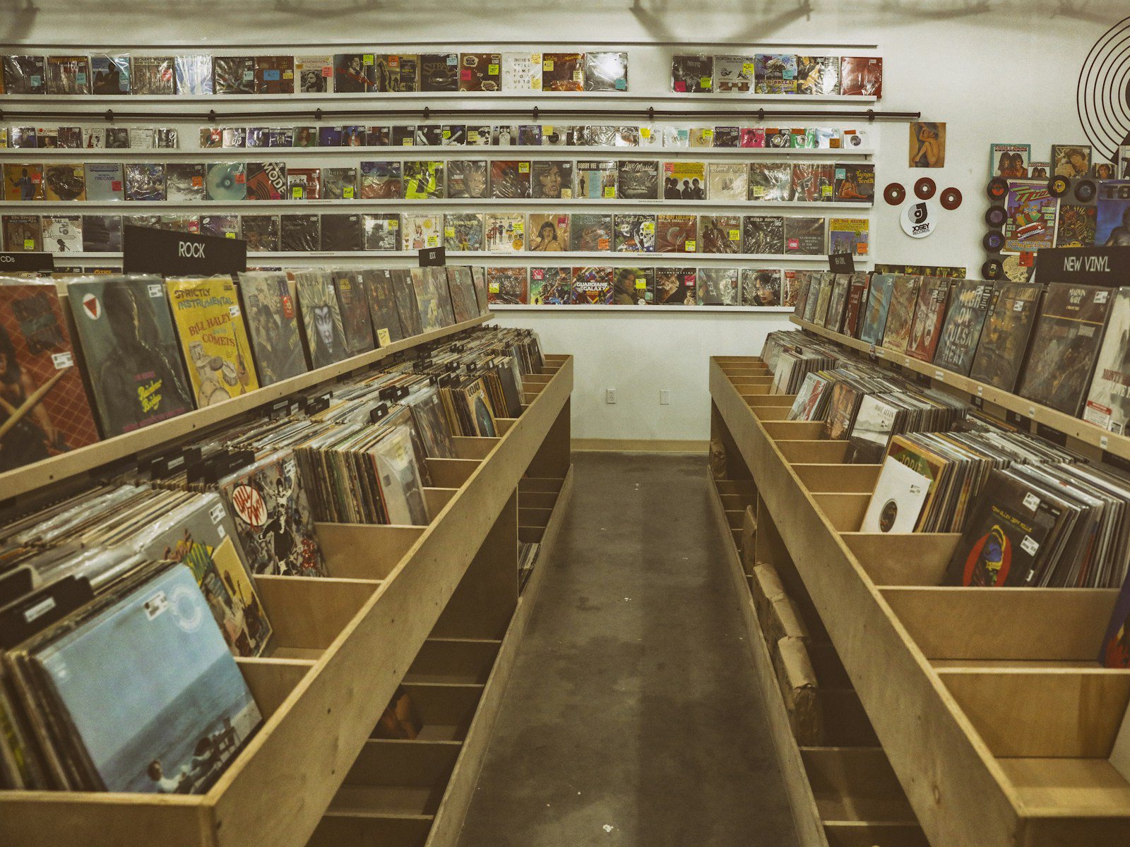 Dim wall of record sleeves with abstract geometric artwork under warm light, no people