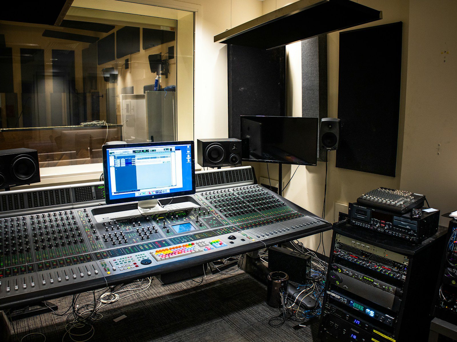 A studio desk at night with a small mixing console, two monitor speakers and a laptop showing an export progress bar, no people